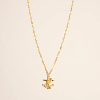 Gold necklace with a small anchor pendant on a beige background
