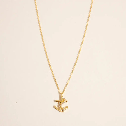 Gold necklace with a small anchor pendant on a beige background