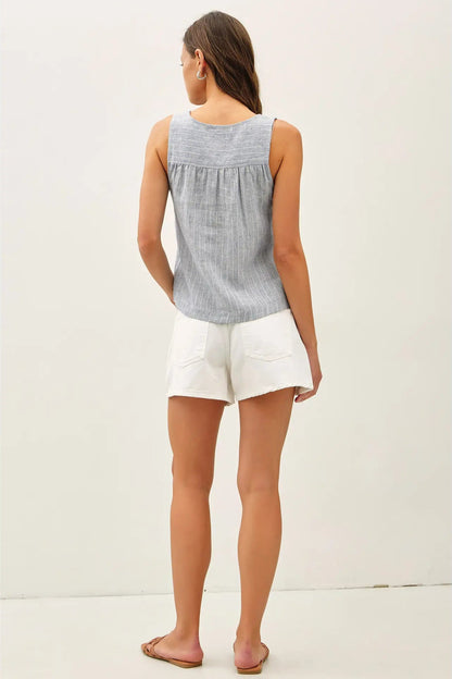 Woman wearing a sleeveless blue and white checkered top and white shorts on a plain background