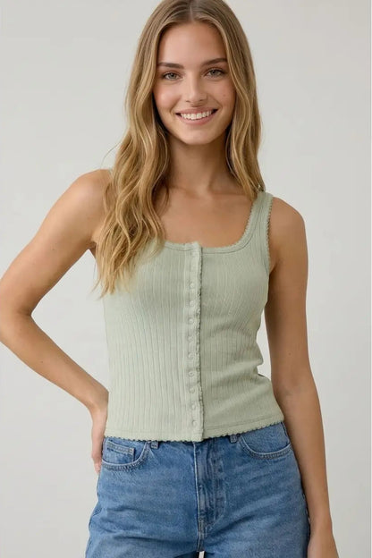 Woman wearing a light green ribbed tank top and blue jeans against a plain background