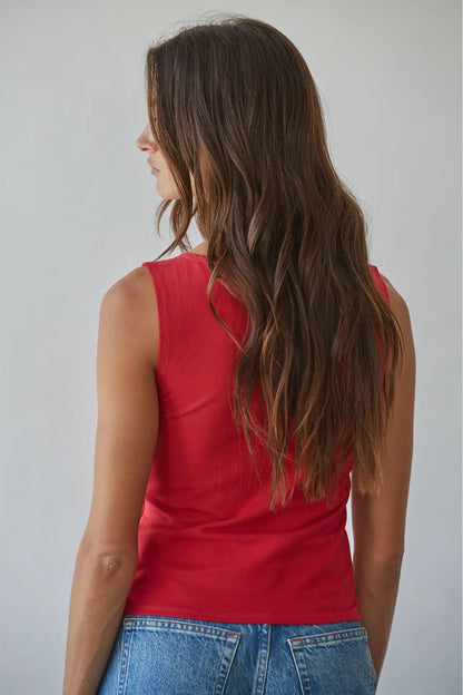 A woman with long brown hair is shown from the back wearing a sleeveless red top and blue jeans against a plain light gray background.