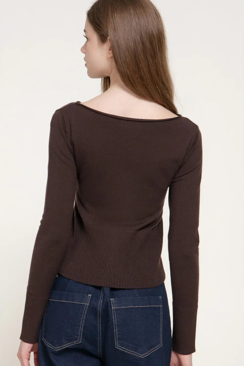 A woman shown from the back wearing a dark brown long-sleeve knit top with a wide boat neckline and dark blue jeans, against a plain off-white background.