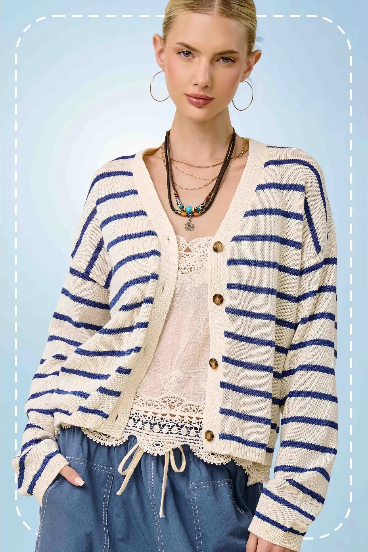 Woman wearing a striped cardigan over a lace top with a blue background