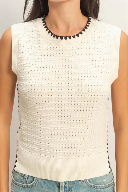 White sleeveless top with black trim worn by a person on a white background