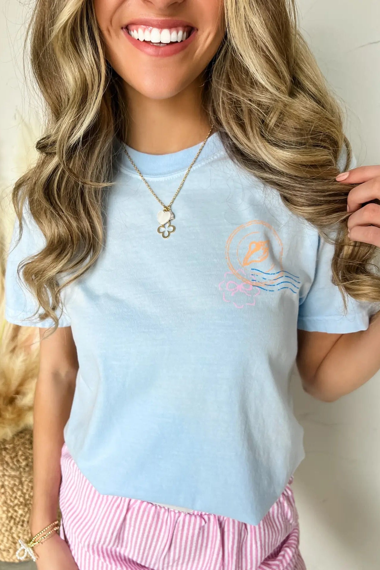 Woman wearing a light blue t-shirt with a graphic design, smiling and holding her hair.