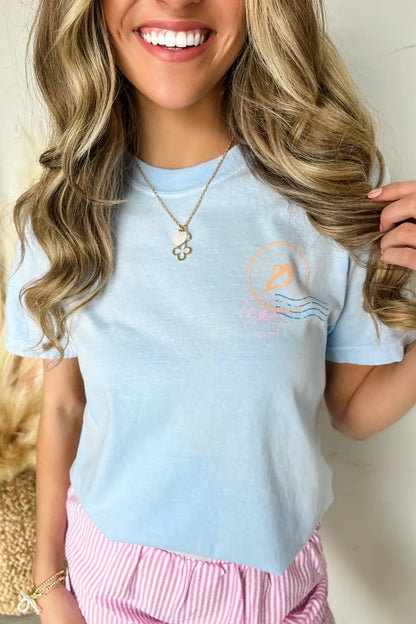 Woman wearing a light blue t-shirt with a graphic design, smiling and holding her hair.