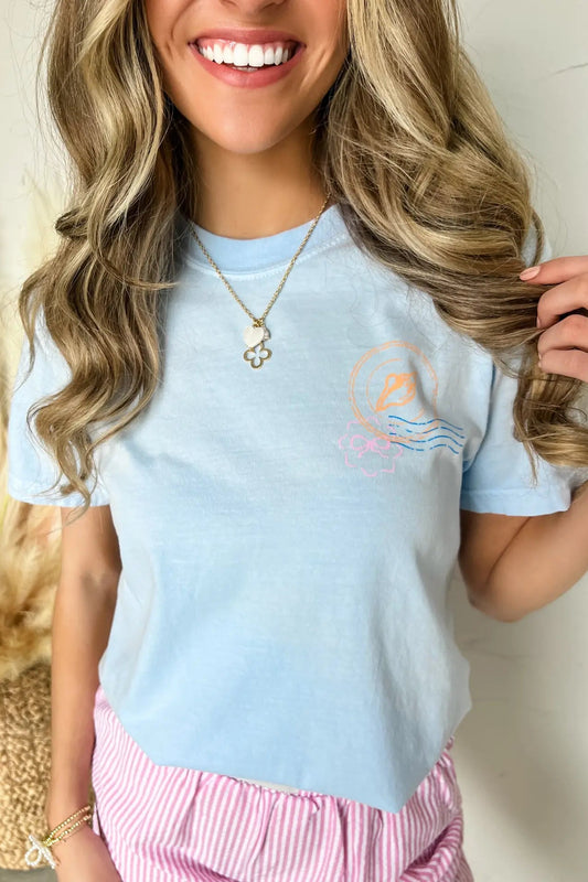Woman wearing a light blue t-shirt with a graphic design, smiling and holding her hair.