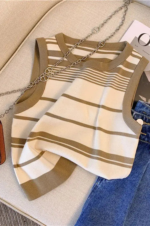 A sleeveless knit top with horizontal beige and brown stripes, styled in a flat lay on a beige sofa with blue jeans, a brown handbag, and a magazine.