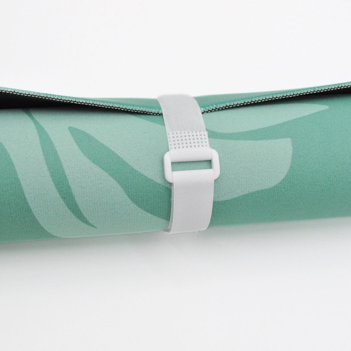 A close-up of a rolled yoga mat in mint green with a tonal leaf pattern, secured with a white plastic strap on a clean white background.