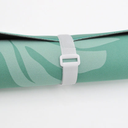 A close-up of a rolled yoga mat in mint green with a tonal leaf pattern, secured with a white plastic strap on a clean white background.