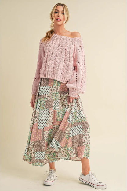 Woman wearing a pink off-shoulder sweater and patterned skirt on a beige background