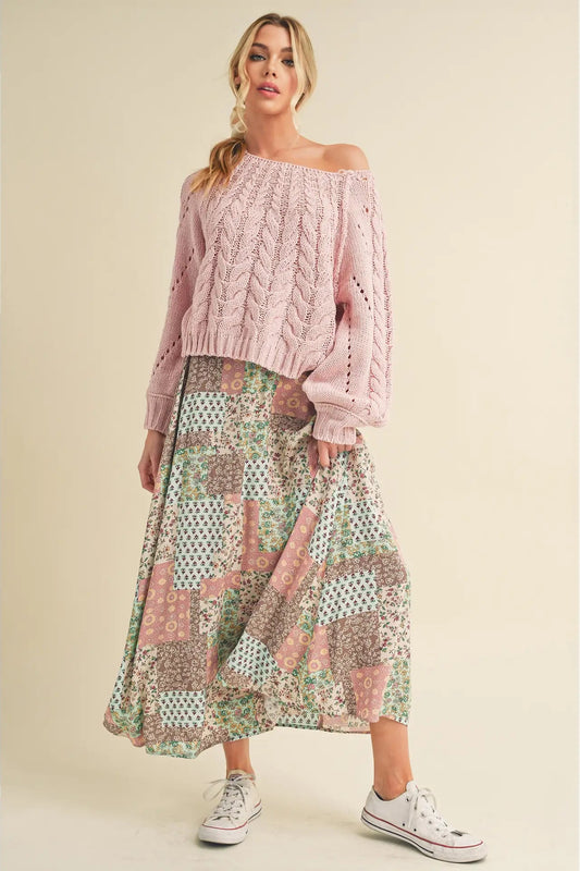 Woman wearing a pink off-shoulder sweater and patterned skirt on a beige background