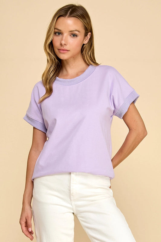 Woman wearing a light purple sweater and white pants against a beige background