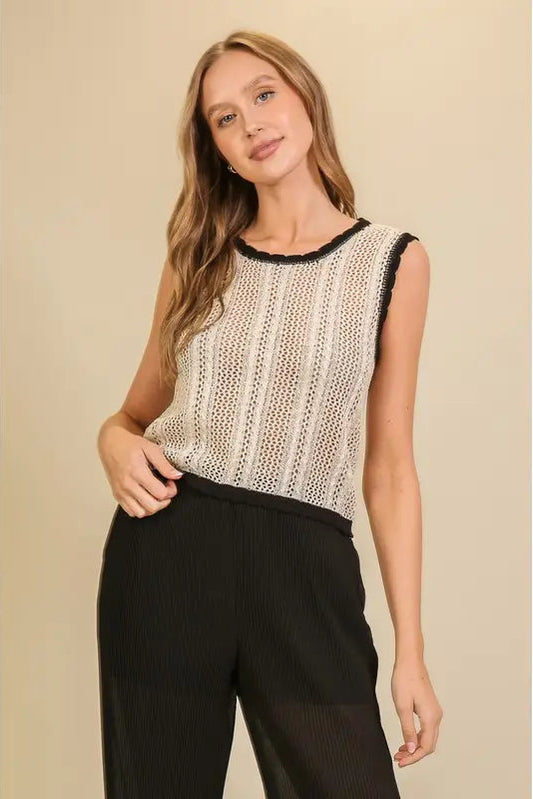 A woman modeling a sleeveless knit top with a cream and black vertical textured pattern and black trim, paired with black pants, against a solid beige background.