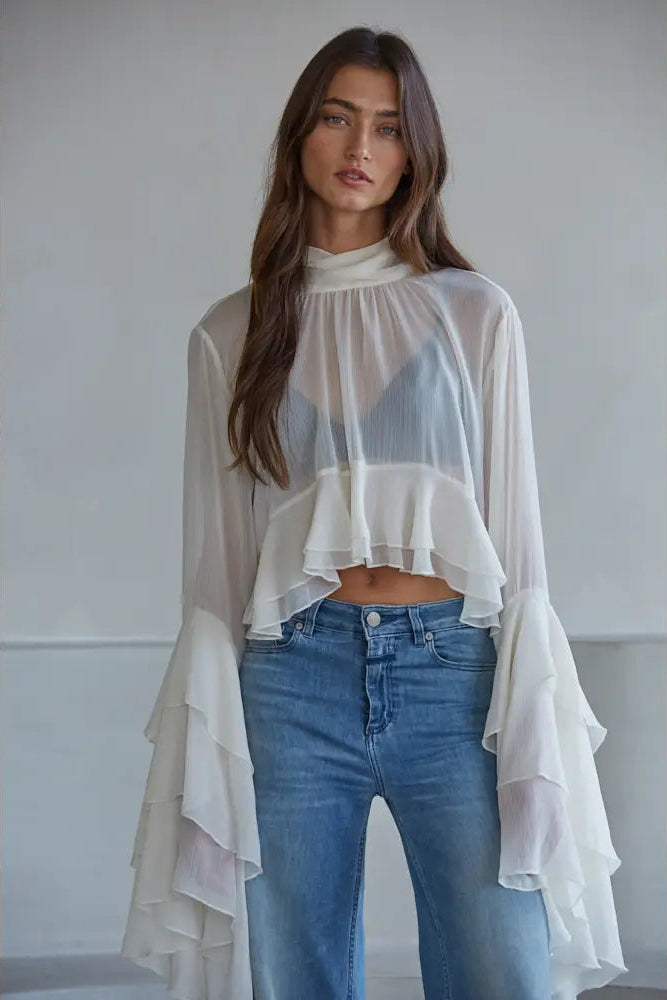 Woman wearing a sheer white top and blue jeans against a plain background