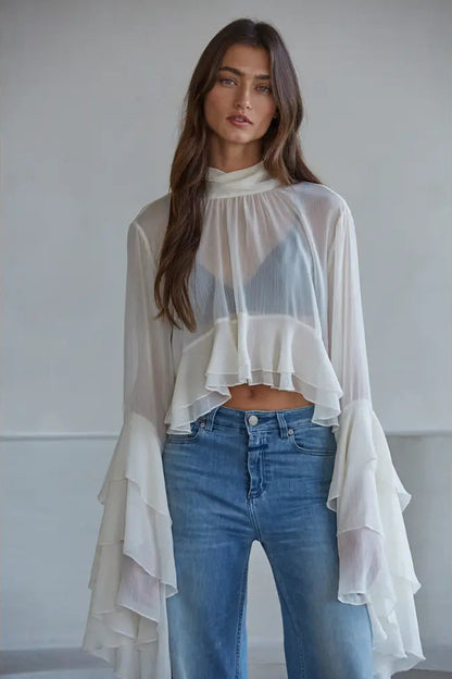 Woman wearing a sheer white top and blue jeans against a plain background