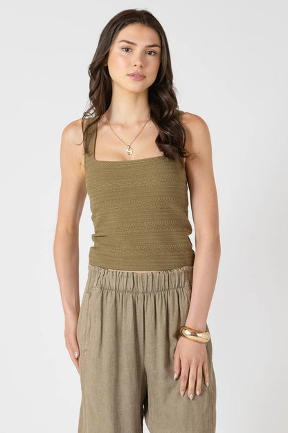 Woman wearing a green tank top and beige pants on a white background