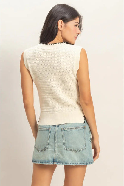 Woman wearing a cream sleeveless top and denim skirt on a plain background