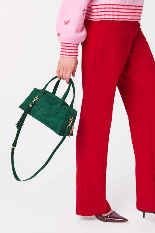 A person wearing bright red wide-leg trousers, a pink sweater with red stripes, and holding a dark green suede handbag with gold hardware against a plain white background.