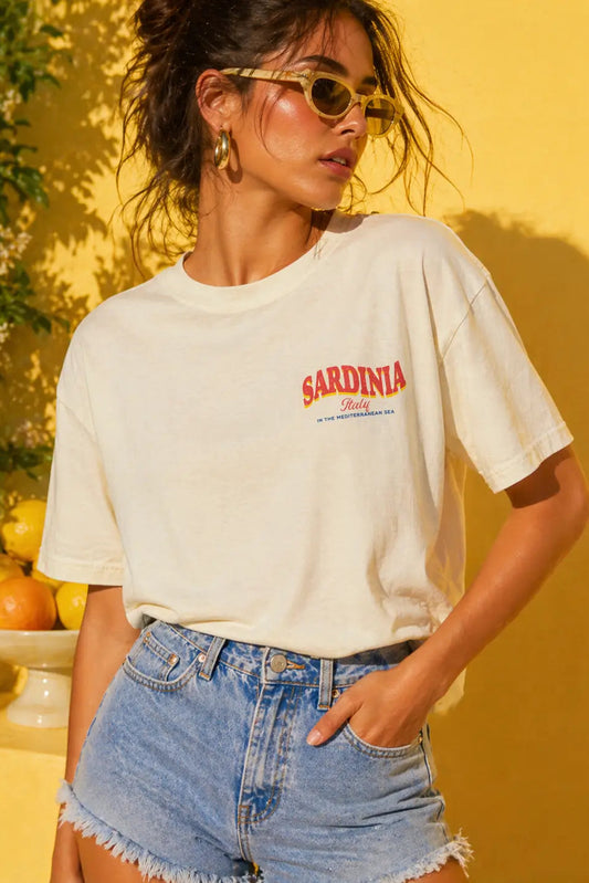 Woman wearing a white t-shirt with 'Sardinia' print against a yellow background