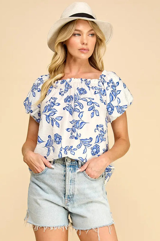 Woman wearing a floral top and denim shorts with a beige background