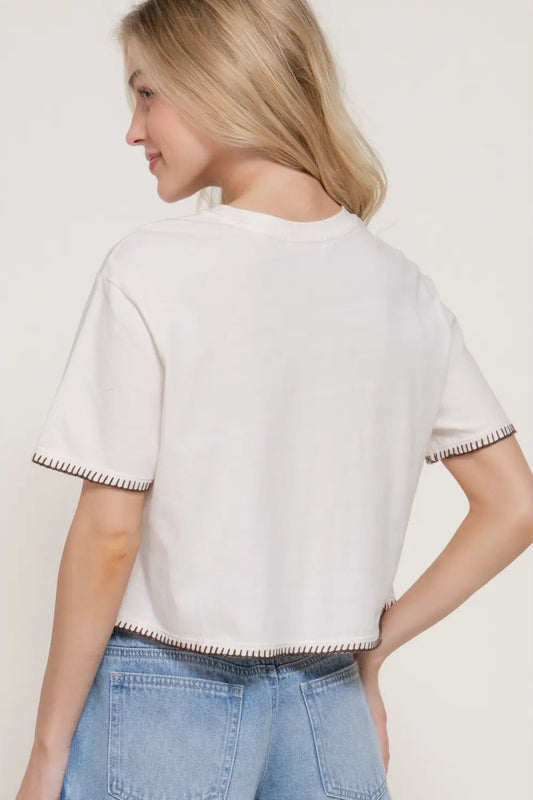 Woman wearing a white short-sleeve top with trim details on a plain background