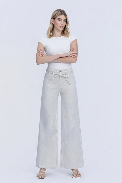 A woman modeling a pair of light gray wide-leg pants with a drawstring waist, paired with a white short-sleeve top, against a plain light gray studio background.