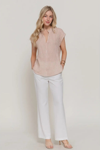 Woman wearing a sleeveless ribbed blouse and light-colored pants on a plain background