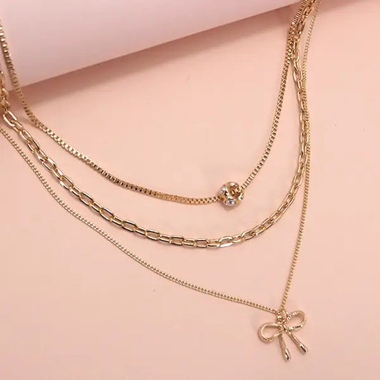 Gold chain necklaces with bow and round charm on a pink background