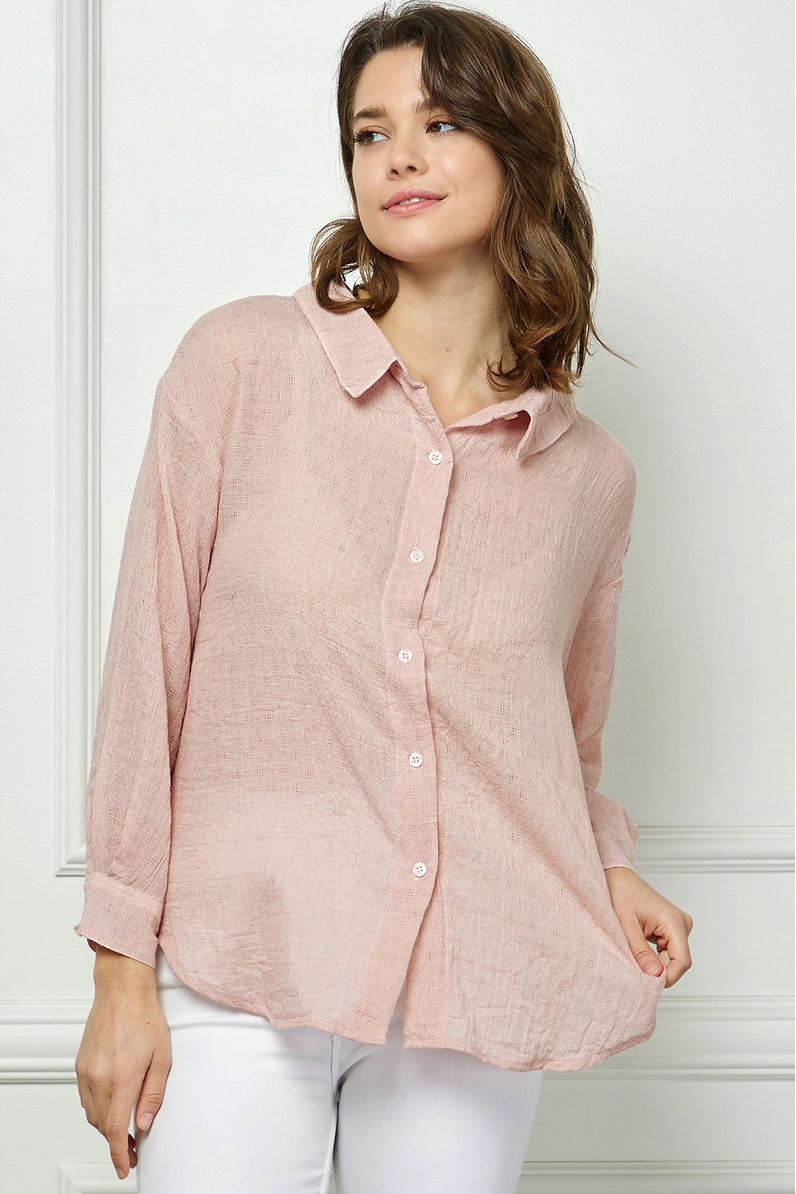 Woman wearing a light pink button-up shirt and white pants against a white background