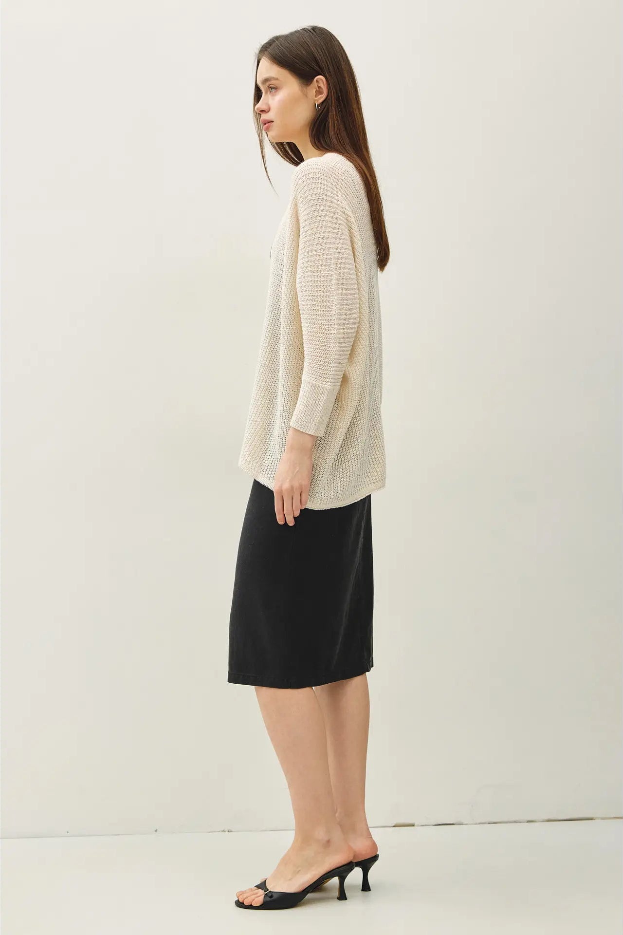 Woman wearing a beige sweater and black skirt against a white background