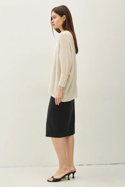 Woman wearing a beige sweater and black skirt against a white background