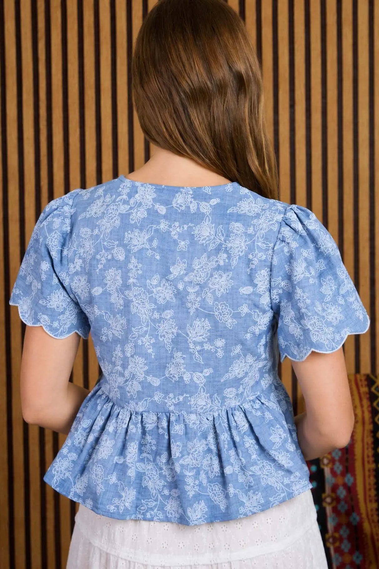 Person wearing a blue floral peplum top against a wooden panel background
