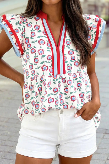 Woman wearing a floral blouse with red and blue accents and white shorts.