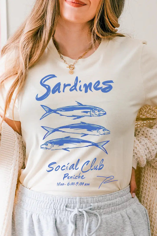 Woman wearing a 'Sardines Social Club' t-shirt with blue fish graphics indoors.