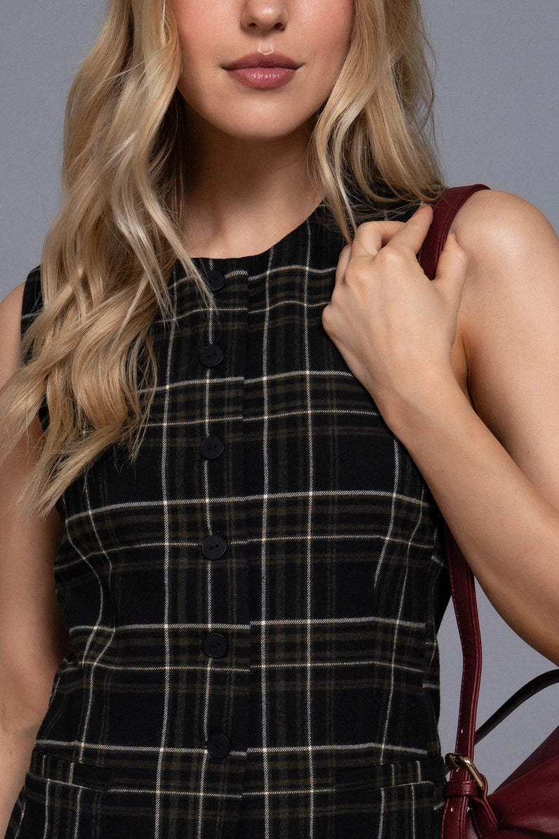 Woman wearing a black plaid dress holding a red handbag against a gray background