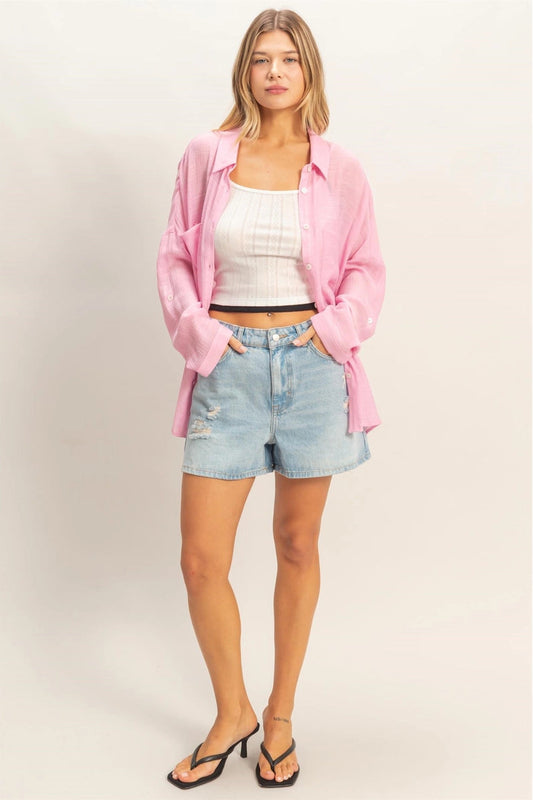 Woman wearing a pink cardigan, white top, and denim shorts on a light background