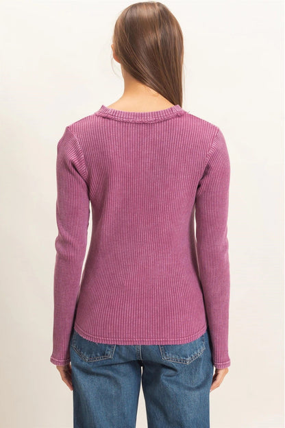 A woman viewed from the back wearing a ribbed long-sleeve knit sweater in a dusty rose pink color, paired with blue jeans, against a plain off-white background.