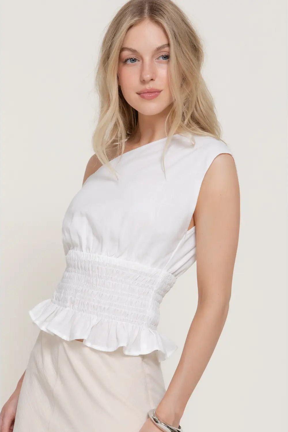 Woman wearing a white one-shoulder top against a plain background