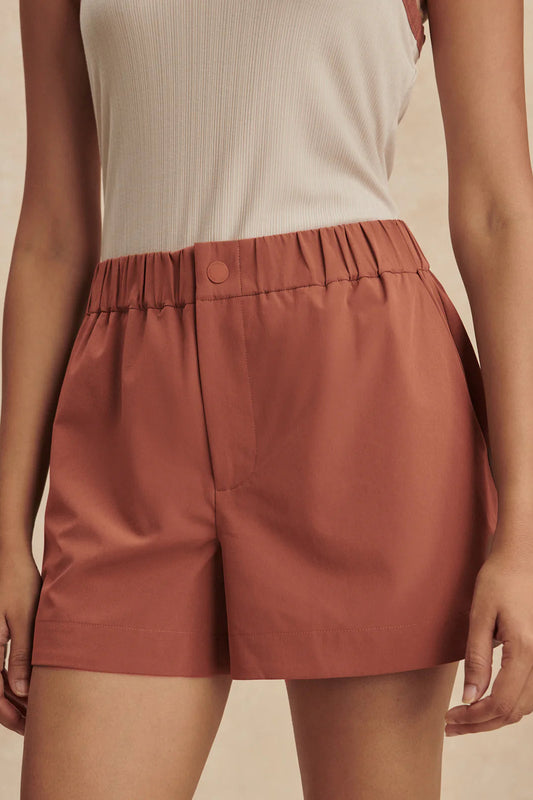 Person wearing rust-colored shorts on a beige background