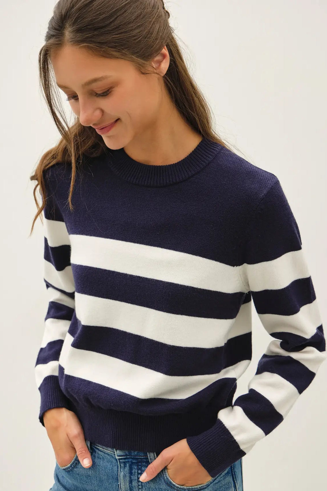 A woman wearing a navy blue and white horizontally striped knit sweater with blue jeans, photographed against a plain light background.