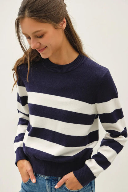 A woman wearing a navy blue and white horizontally striped knit sweater with blue jeans, photographed against a plain light background.