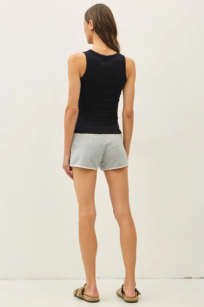 A woman shown from the back wearing a black ribbed tank top and light gray heathered shorts, standing against a plain off-white studio background.