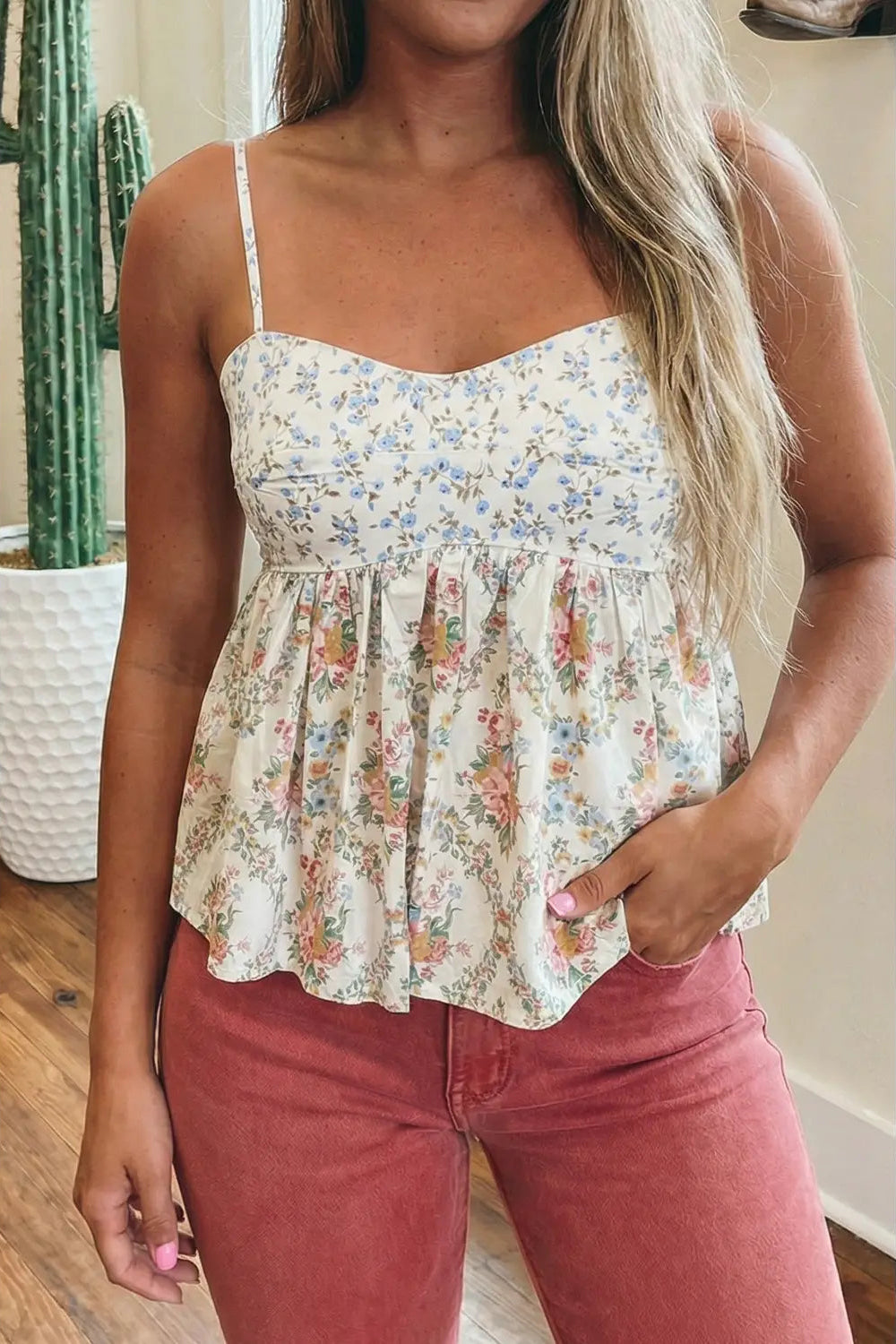 Woman wearing a floral top and pink pants indoors with a cactus plant in the background.