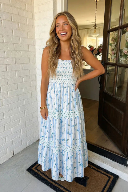 Woman in a floral dress standing in front of a white brick wall.