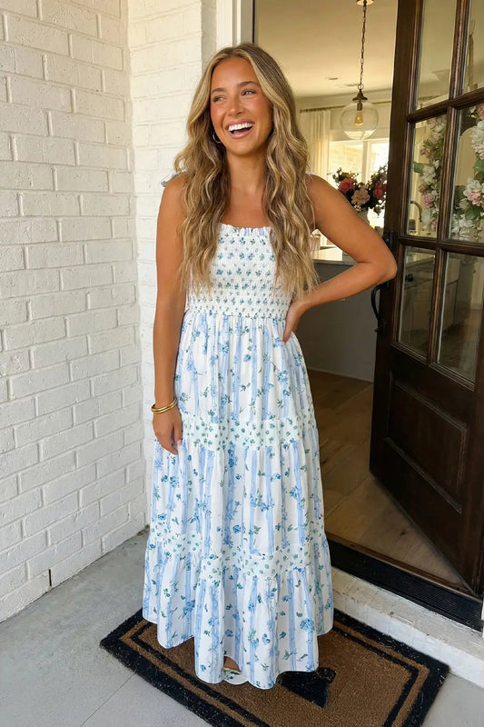 Woman in a floral dress standing in front of a white brick wall.