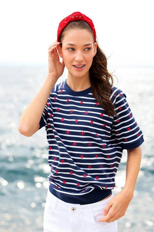 Woman wearing a navy and white striped shirt with red accents by the water