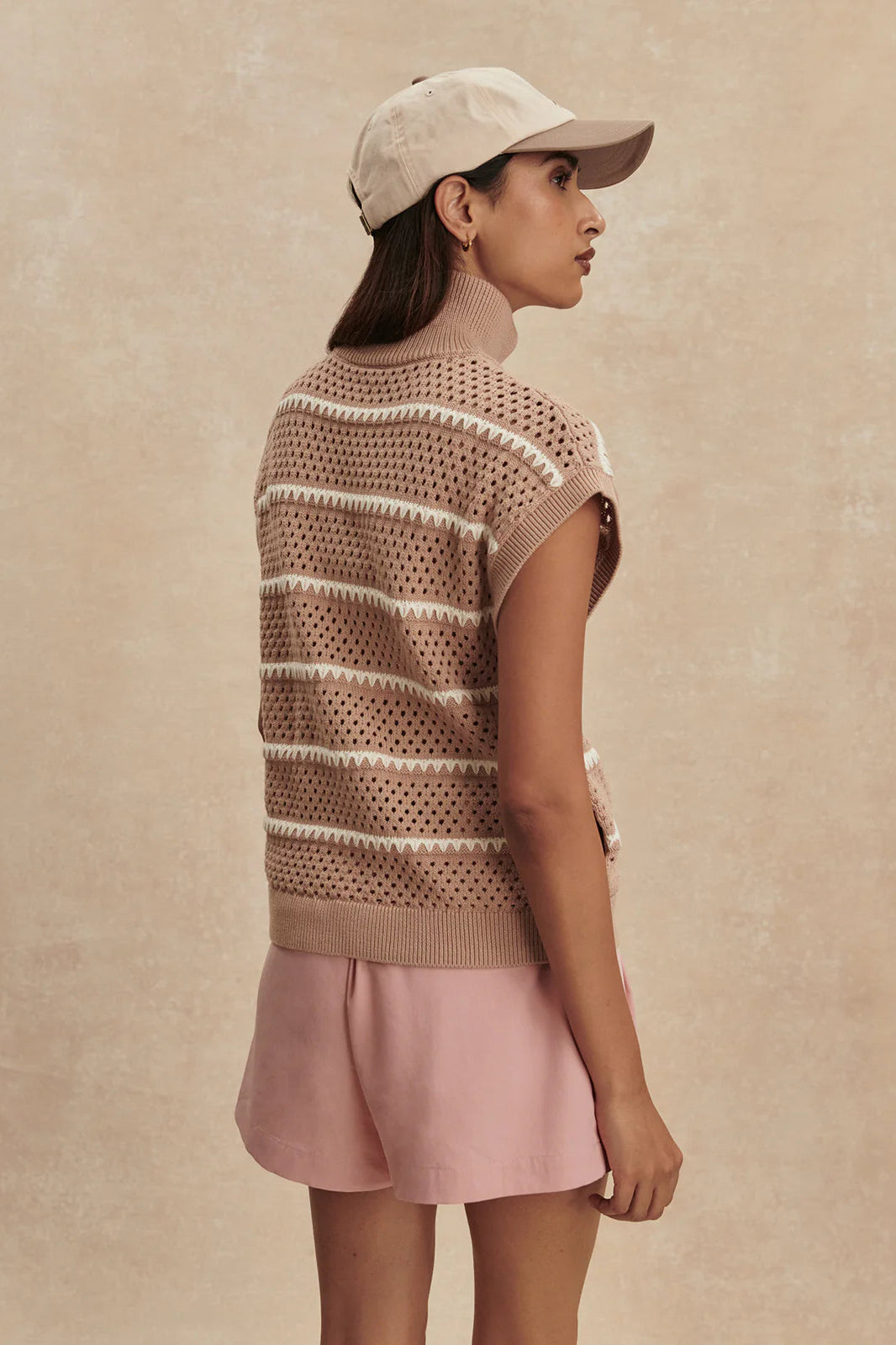 Woman wearing a patterned vest and pink skirt against a beige background