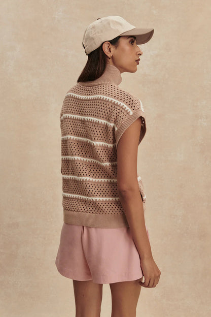 Woman wearing a patterned vest and pink skirt against a beige background