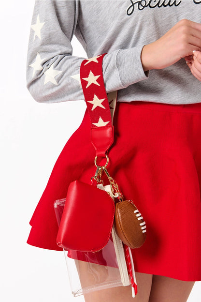 Person wearing a gray sweatshirt and red skirt with a red bag featuring star strap and football charm.